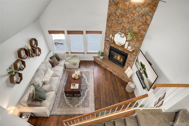 living room featuring vaulted ceiling, a stone fireplace, and dark hardwood / wood-style flooring