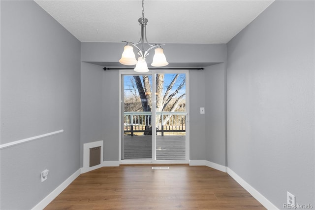 unfurnished dining area featuring a notable chandelier, wood-type flooring, and a textured ceiling