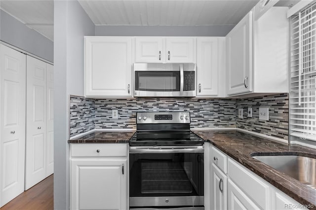 kitchen with white cabinetry, dark stone countertops, dark hardwood / wood-style floors, stainless steel appliances, and backsplash