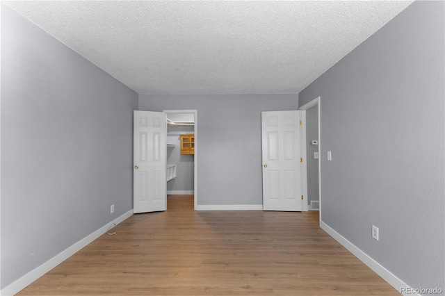 unfurnished bedroom with a walk in closet, a closet, a textured ceiling, and light wood-type flooring