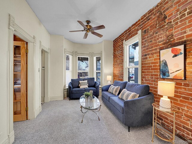 carpeted living area featuring baseboards, brick wall, and ceiling fan