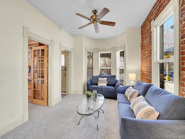 carpeted living area featuring baseboards, brick wall, and a ceiling fan