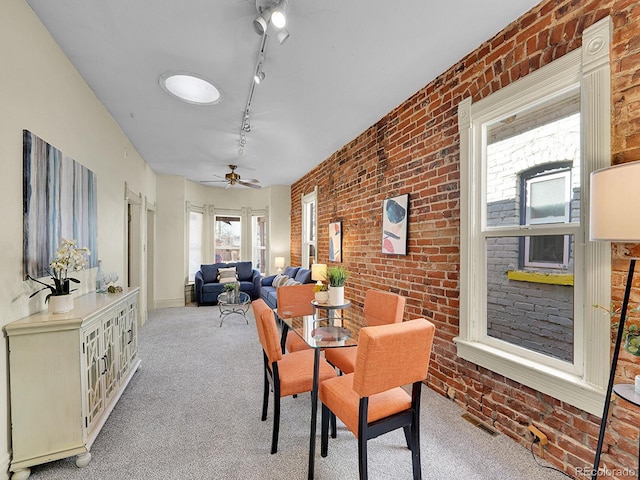 carpeted dining space featuring track lighting, brick wall, a ceiling fan, and visible vents