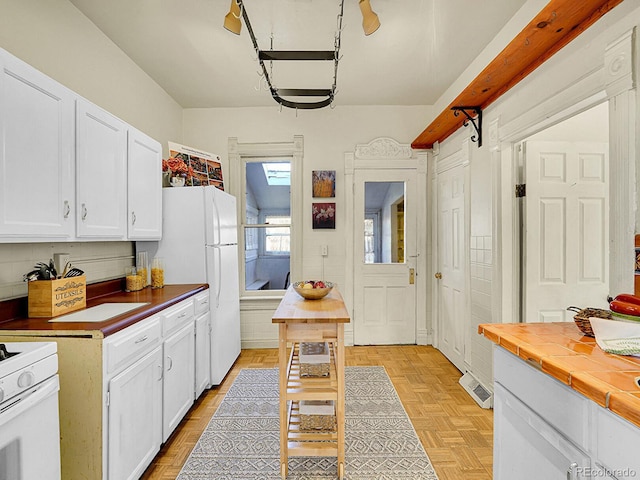 kitchen with white appliances, white cabinets, visible vents, and tile countertops