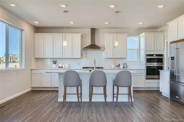 kitchen featuring white cabinets, stainless steel appliances, hanging light fixtures, and wall chimney exhaust hood