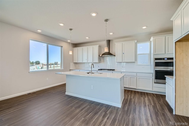 kitchen with white cabinets, decorative light fixtures, stainless steel double oven, and wall chimney range hood