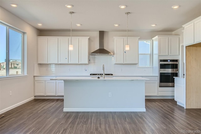 kitchen featuring stainless steel appliances, white cabinetry, hanging light fixtures, and wall chimney exhaust hood