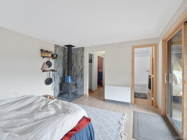 bedroom featuring a wood stove, ensuite bathroom, and light hardwood / wood-style floors