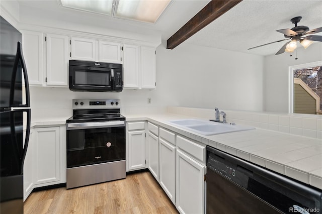 kitchen with light wood finished floors, white cabinets, a sink, black appliances, and beam ceiling