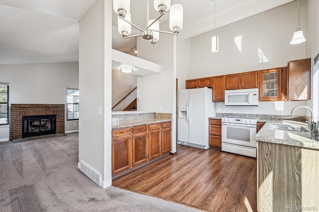 kitchen featuring white appliances, light stone counters, brown cabinets, and a sink