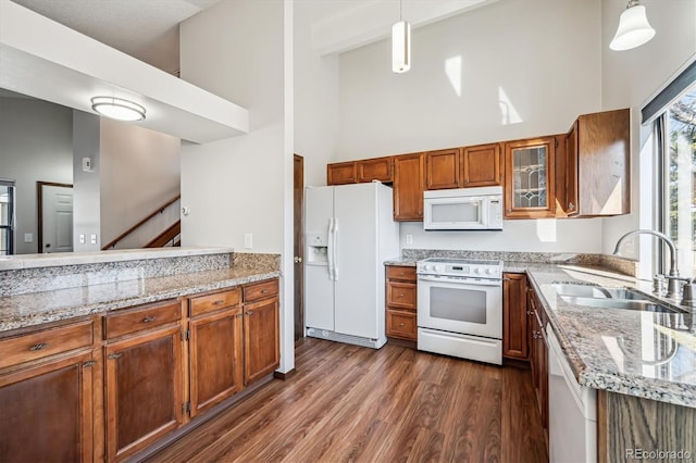 kitchen with white appliances, a high ceiling, brown cabinetry, and a sink