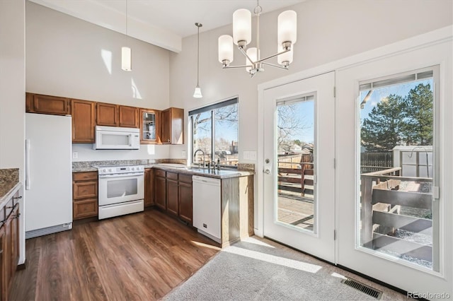 kitchen with white appliances, visible vents, brown cabinetry, dark wood finished floors, and hanging light fixtures