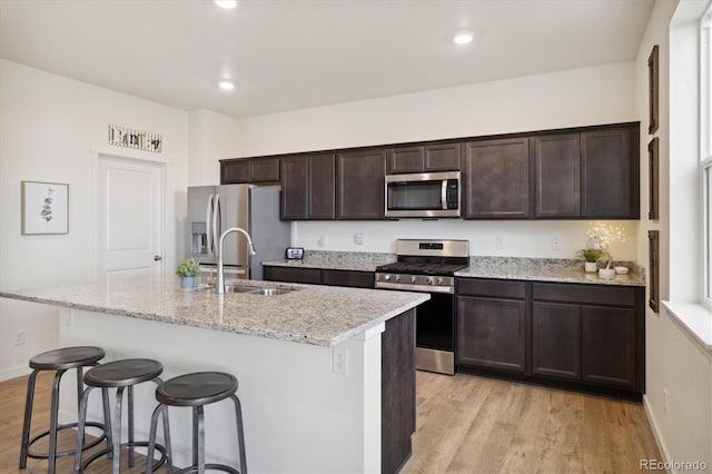 353 Raven Ln, Johnstown, CO 80534 - kitchen with appliances with stainless steel finishes, a sink, light wood finished floors, a kitchen breakfast bar, and dark brown cabinets