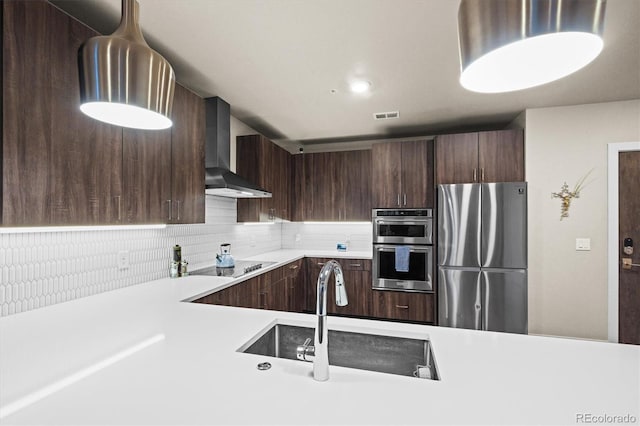 kitchen featuring sink, dark brown cabinets, wall chimney range hood, stainless steel appliances, and backsplash