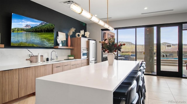 kitchen featuring light tile patterned flooring, a kitchen island, appliances with stainless steel finishes, pendant lighting, and sink