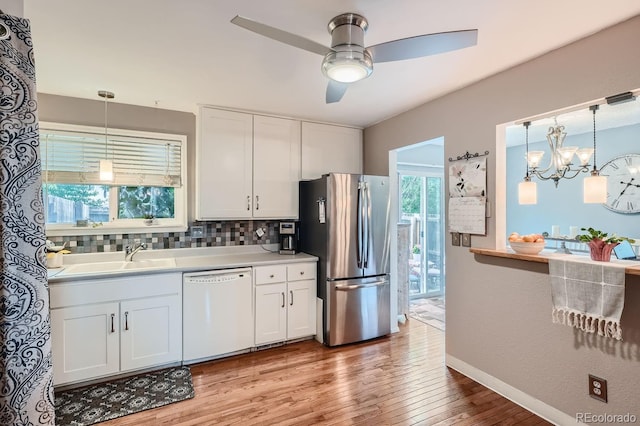 kitchen with stainless steel refrigerator, ceiling fan with notable chandelier, white dishwasher, and white cabinetry