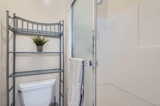 bathroom featuring a shower with shower door and toilet