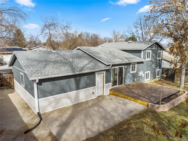 exterior space with a shingled roof, a patio, a wooden deck, and fence