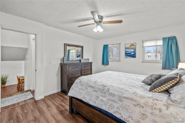 bedroom featuring a ceiling fan, a textured ceiling, baseboards, and wood finished floors