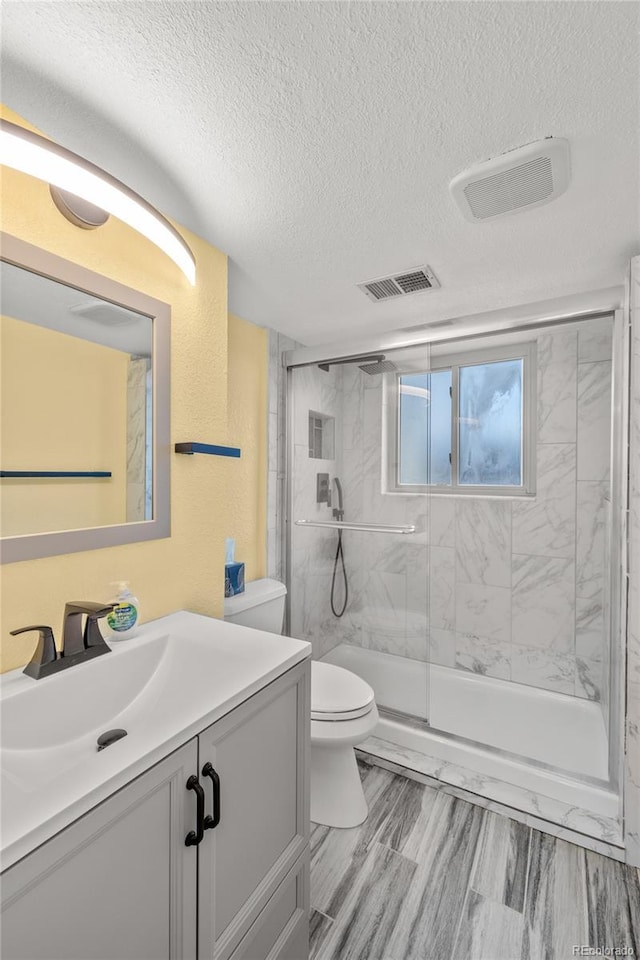 full bathroom with a marble finish shower, visible vents, toilet, a textured ceiling, and vanity