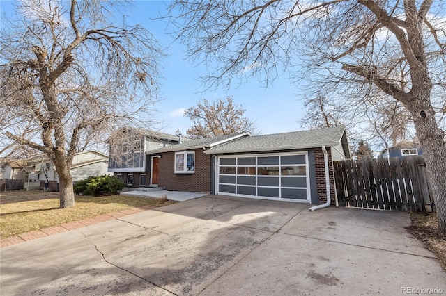 tri-level home featuring driveway, roof with shingles, an attached garage, fence, and brick siding