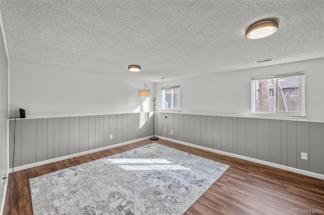 spare room with a textured ceiling, wainscoting, wood finished floors, and visible vents