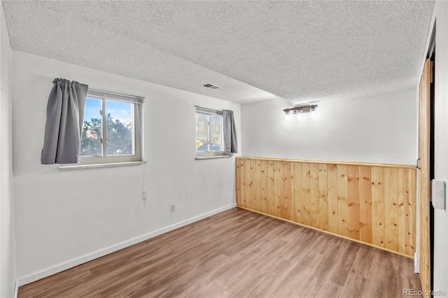 unfurnished room featuring visible vents, wood walls, a textured ceiling, wood finished floors, and baseboards