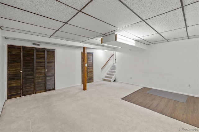 finished basement featuring light colored carpet, a paneled ceiling, visible vents, and stairs