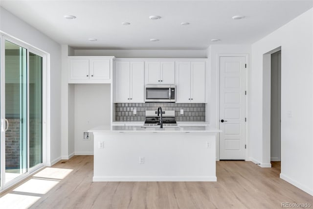 kitchen featuring white cabinets, backsplash, stainless steel appliances, and an island with sink