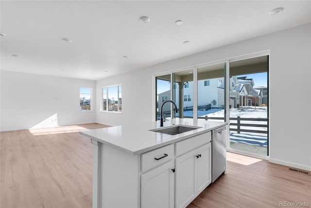 kitchen with light wood-type flooring, sink, a center island with sink, dishwasher, and white cabinetry