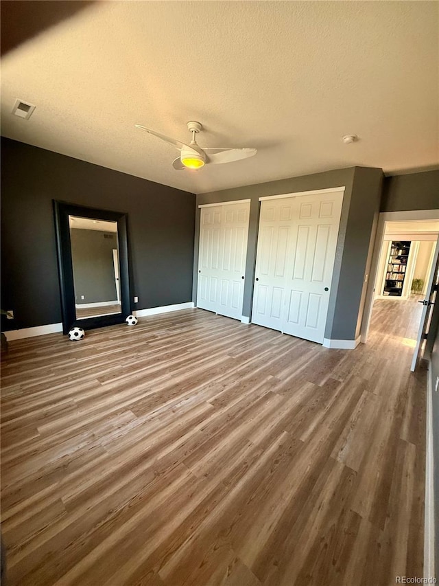 653 Glenarbor Cir, Longmont, CO 80504 - unfurnished bedroom with two closets, wood finished floors, baseboards, a textured ceiling, and a ceiling fan