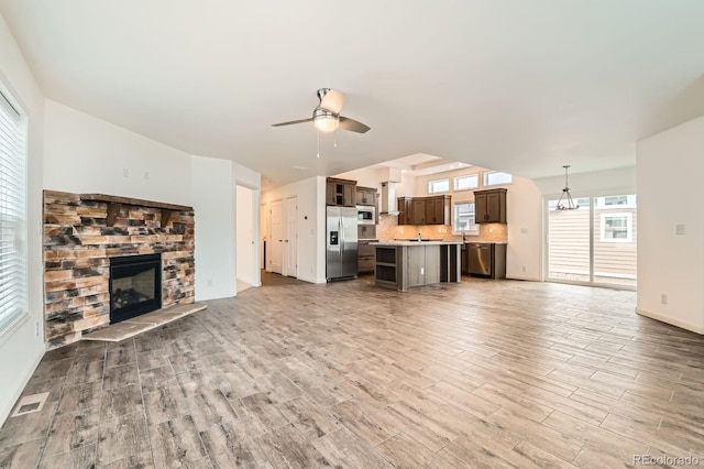 6261 Red Cedar St, Frederick, CO 80530 - unfurnished living room with ceiling fan with notable chandelier, a stone fireplace, visible vents, and wood finished floors