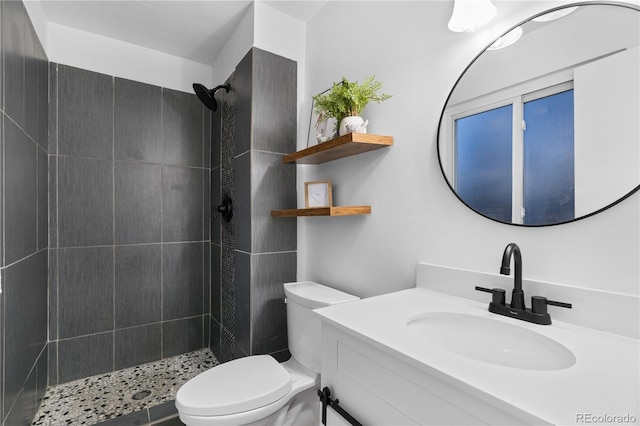 bathroom with a tile shower, vanity, and toilet