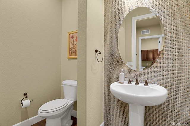 bathroom featuring decorative backsplash, toilet, sink, and tile walls