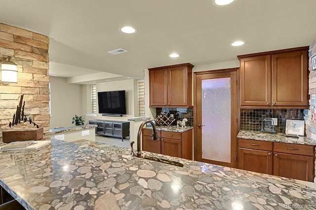 kitchen featuring light stone countertops, sink, backsplash, and kitchen peninsula