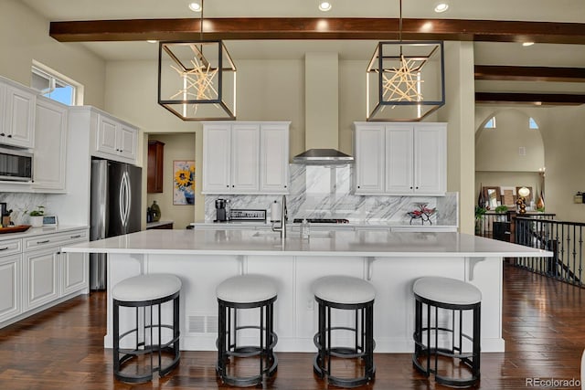 kitchen featuring appliances with stainless steel finishes, a breakfast bar, an island with sink, white cabinets, and wall chimney range hood