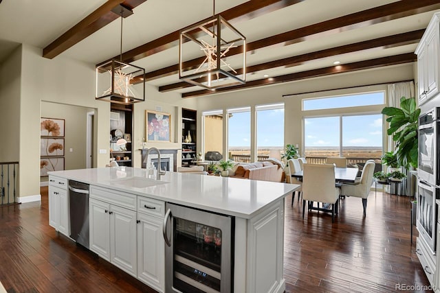 kitchen with wine cooler, white cabinetry, hanging light fixtures, stainless steel dishwasher, and an island with sink