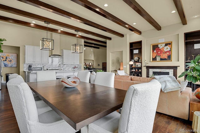 dining area with a stone fireplace, sink, dark hardwood / wood-style flooring, a chandelier, and beam ceiling