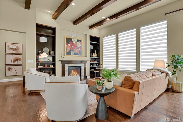 living room featuring beam ceiling, hardwood / wood-style flooring, built in features, and a fireplace