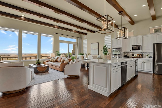 kitchen with pendant lighting, appliances with stainless steel finishes, white cabinetry, beam ceiling, and a center island with sink