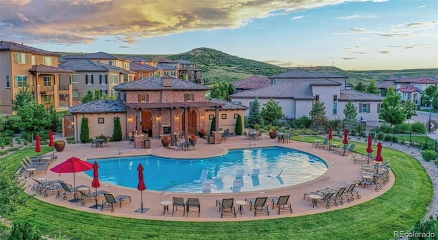 pool at dusk featuring a patio, a mountain view, and a lawn