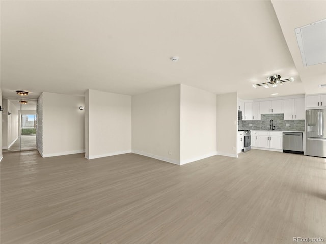 unfurnished living room with baseboards, a sink, and light wood-type flooring