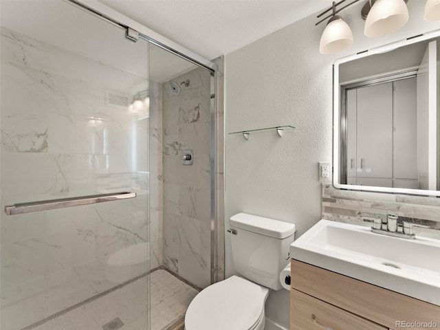 bathroom featuring a marble finish shower, a textured wall, vanity, and toilet