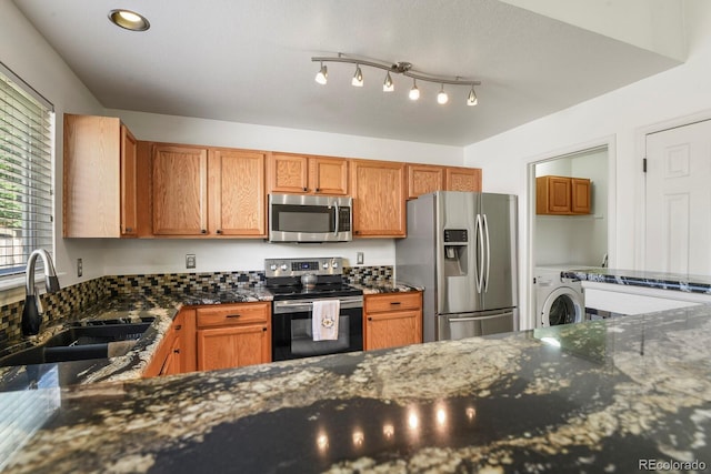 kitchen with dark stone counters, sink, stainless steel appliances, and washer / dryer