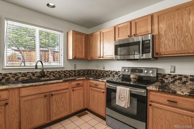 kitchen featuring light tile patterned flooring, sink, appliances with stainless steel finishes, and dark stone counters