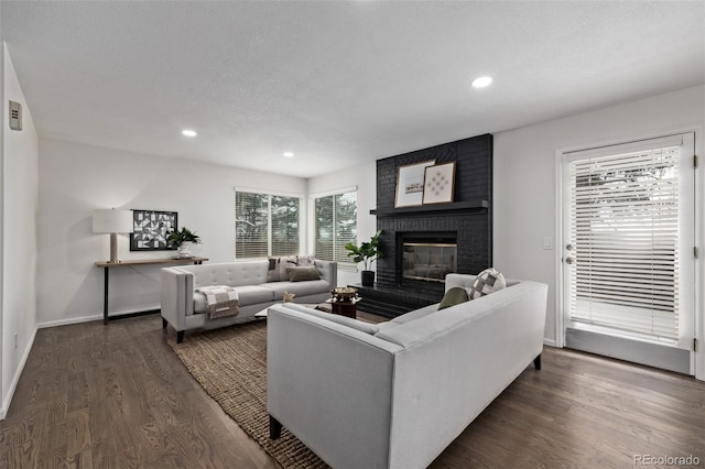 living room featuring a brick fireplace, dark hardwood / wood-style floors, and a textured ceiling