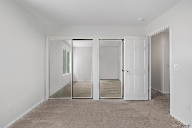 unfurnished bedroom featuring two closets and light carpet