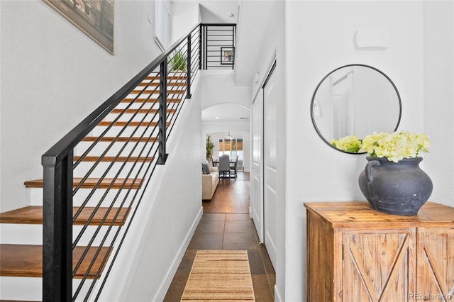 interior space featuring arched walkways, baseboards, stairs, a high ceiling, and dark tile patterned floors