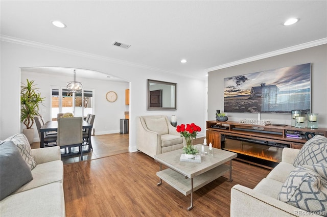 living room with arched walkways, crown molding, visible vents, a glass covered fireplace, and wood finished floors