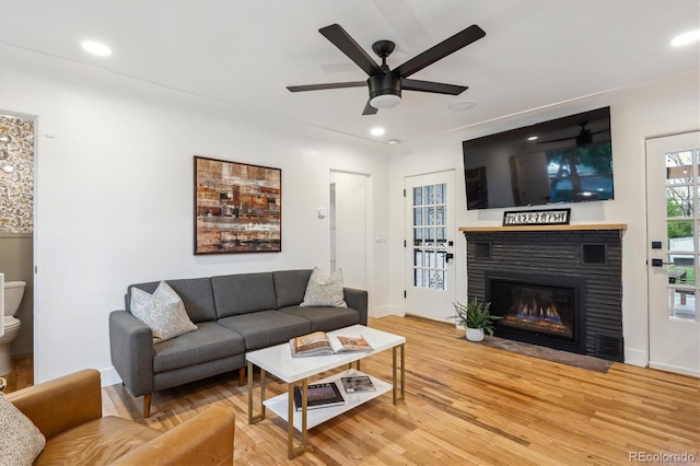 living room featuring a ceiling fan, light wood-style floors, a fireplace with flush hearth, baseboards, and recessed lighting